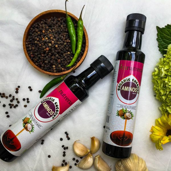 Bottles of Econutrena Coconut Aminos with a tropical background, showcasing the organic seasoning's rich, dark color and natural ingredients.